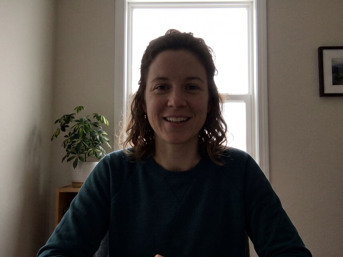 A woman on a video call with a bright window behind her. Her face is in shadow.